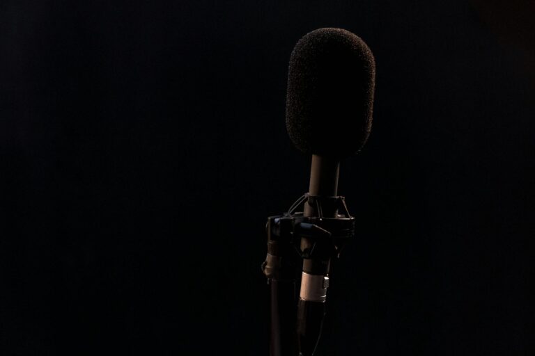 Close-up of a condenser microphone on a mic stand with a black background, perfect for audio production themes.