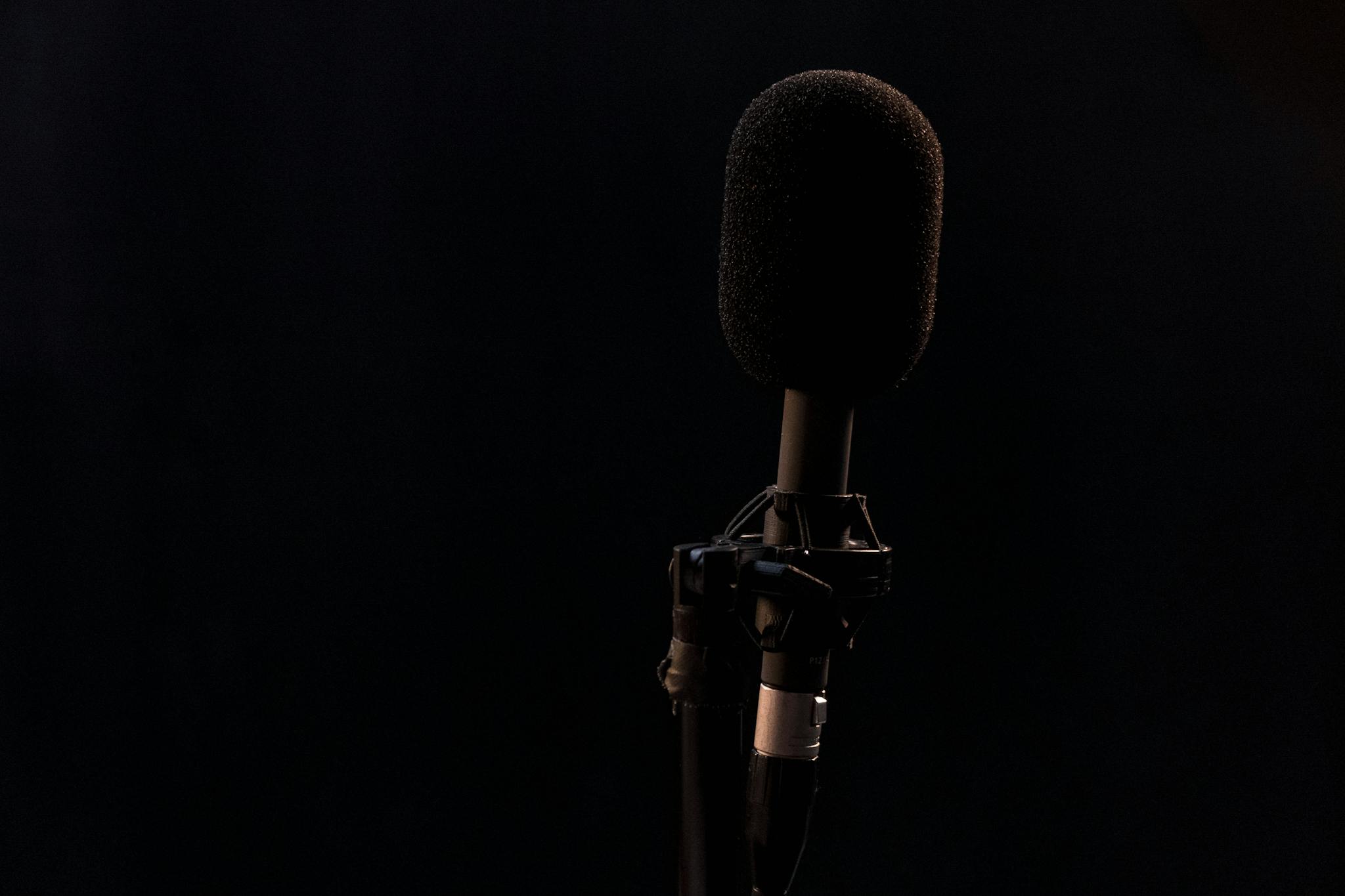 Close-up of a condenser microphone on a mic stand with a black background, perfect for audio production themes.