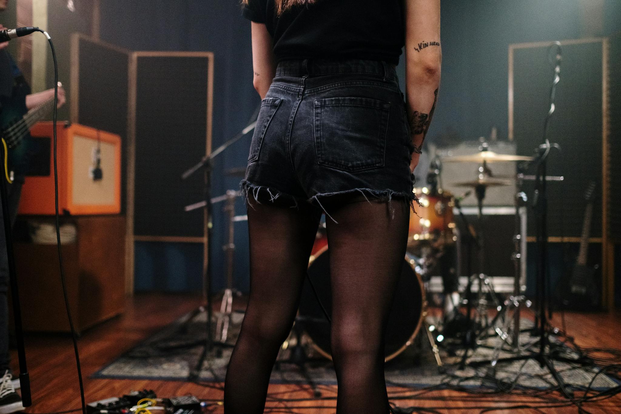 Woman standing with drum kit and microphone in music rehearsal space.
